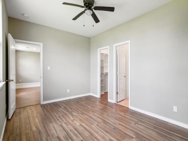 unfurnished bedroom featuring a walk in closet, baseboards, wood finished floors, a closet, and a ceiling fan