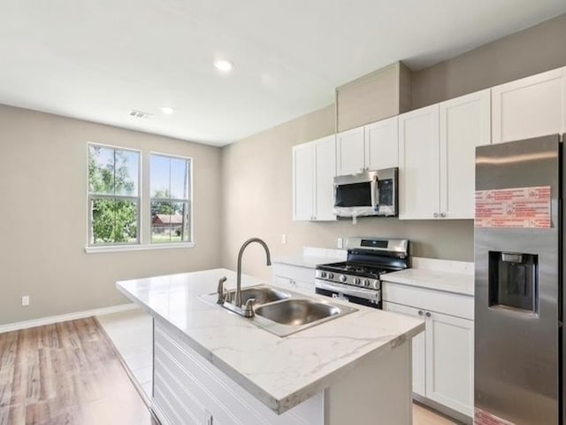 kitchen featuring baseboards, a center island with sink, a sink, appliances with stainless steel finishes, and white cabinetry