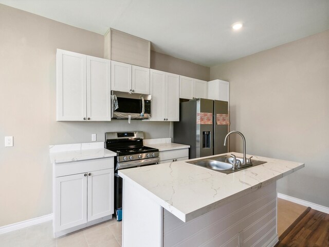 kitchen with a sink, appliances with stainless steel finishes, a kitchen island with sink, and white cabinetry