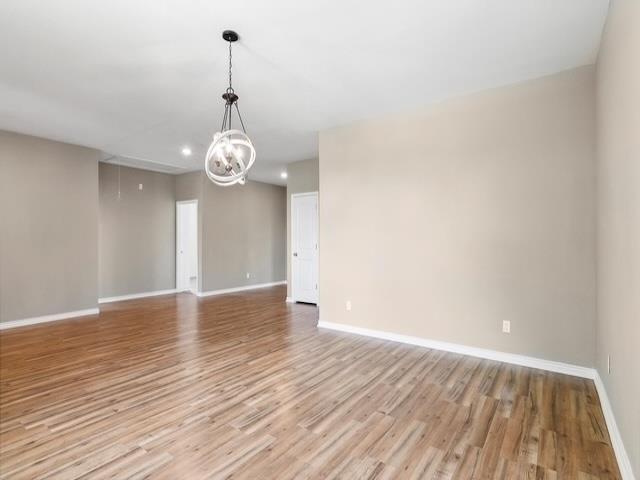 empty room featuring an inviting chandelier, light wood-style flooring, recessed lighting, and baseboards