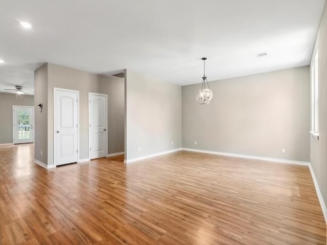 empty room with baseboards, ceiling fan with notable chandelier, and light wood finished floors