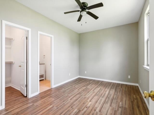 unfurnished bedroom featuring a spacious closet, wood finished floors, baseboards, and a closet