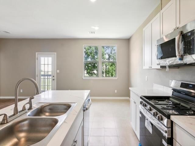 kitchen with a sink, stainless steel appliances, white cabinets, light tile patterned floors, and baseboards