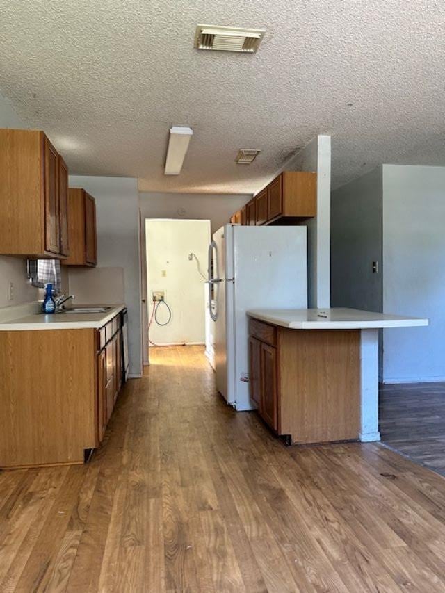 kitchen featuring kitchen peninsula, a textured ceiling, white fridge, and light hardwood / wood-style floors