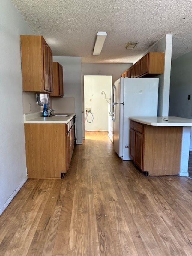 kitchen with white fridge, light wood-type flooring, kitchen peninsula, and a textured ceiling