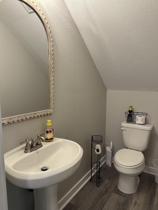 bathroom with baseboards, wood finished floors, toilet, lofted ceiling, and a sink