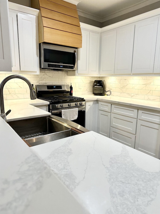 kitchen featuring decorative backsplash, white cabinets, crown molding, appliances with stainless steel finishes, and a sink