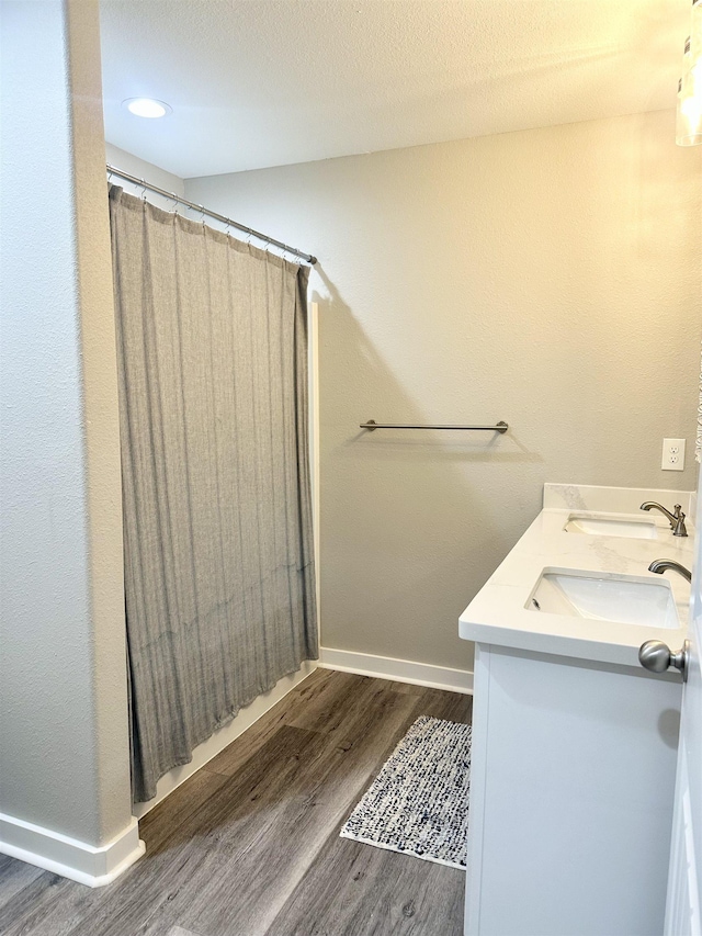 full bath with a shower with shower curtain, baseboards, a sink, double vanity, and wood finished floors