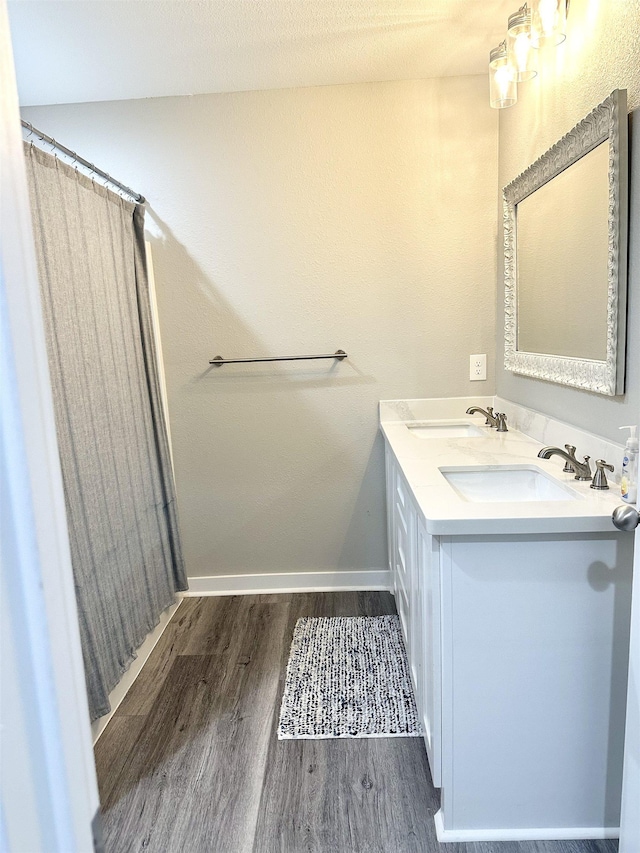 bathroom featuring baseboards, wood finished floors, double vanity, and a sink