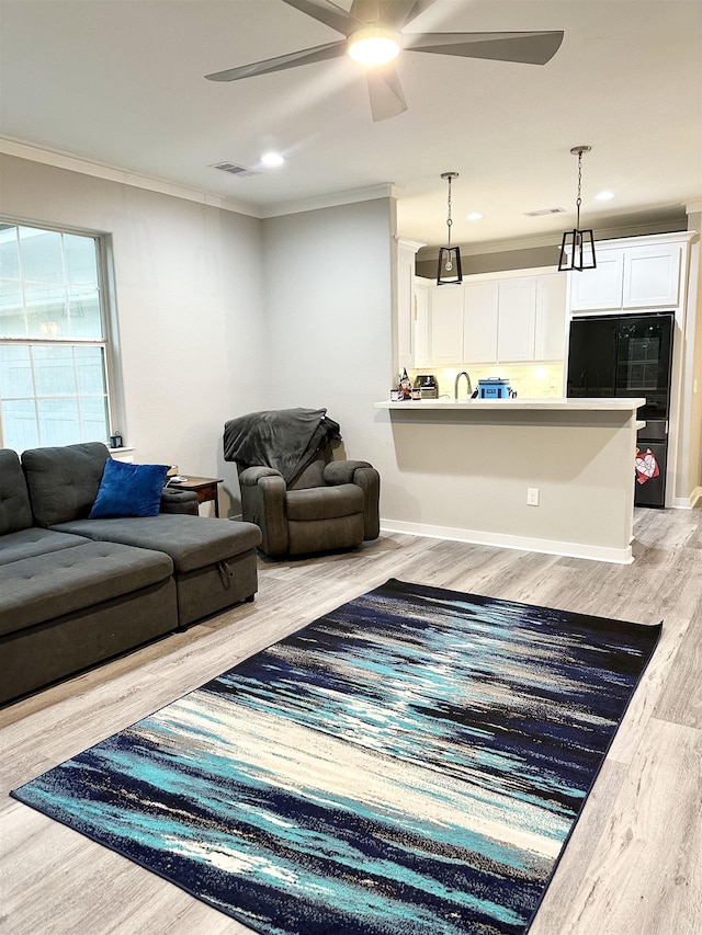living room featuring visible vents, baseboards, ornamental molding, ceiling fan, and light wood-style floors