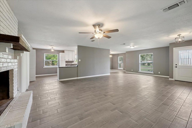 2024 International Ave, Orange, TX 77632 - unfurnished living room with a ceiling fan, a textured ceiling, a brick fireplace, and wood finished floors