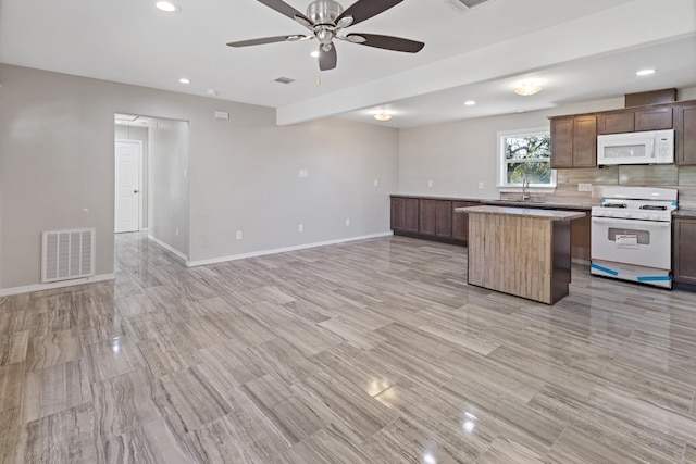 kitchen with backsplash, white appliances, ceiling fan, sink, and a center island