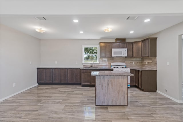 kitchen with tasteful backsplash, light stone counters, white appliances, dark brown cabinetry, and sink