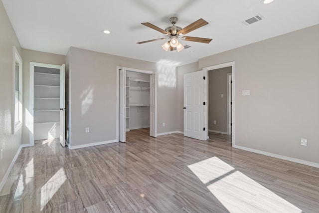 unfurnished bedroom featuring light wood-type flooring, a walk in closet, a closet, and ceiling fan