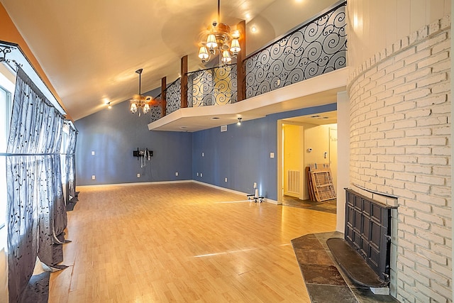 unfurnished living room featuring an inviting chandelier, high vaulted ceiling, and hardwood / wood-style flooring