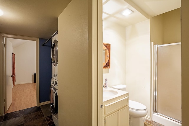 bathroom featuring vanity, toilet, an enclosed shower, and stacked washer and clothes dryer