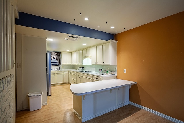 kitchen featuring light wood-type flooring, kitchen peninsula, a breakfast bar area, and gas cooktop