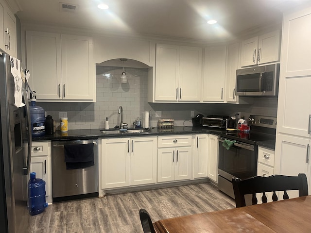 kitchen featuring visible vents, a sink, wood finished floors, dark countertops, and appliances with stainless steel finishes