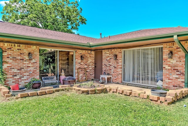 doorway to property featuring brick siding, a lawn, and roof with shingles