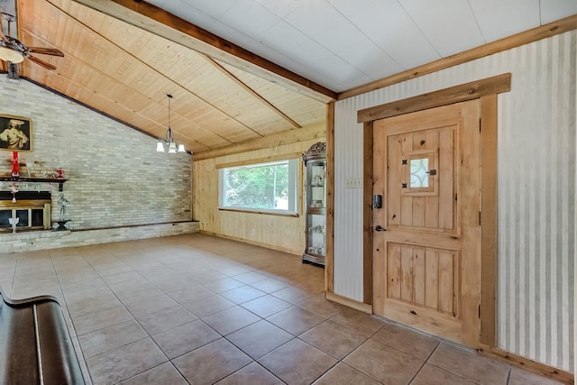 tiled entryway featuring brick wall, a brick fireplace, baseboards, a ceiling fan, and a chandelier