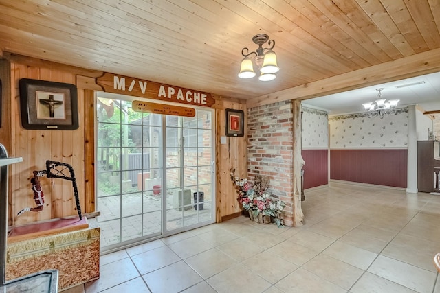 doorway featuring a chandelier, wood walls, wallpapered walls, baseboards, and wainscoting