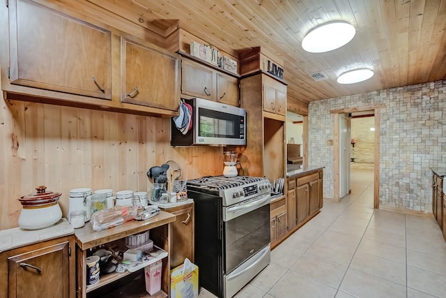 kitchen with stainless steel appliances, light tile patterned flooring, wood ceiling, brown cabinetry, and wood walls