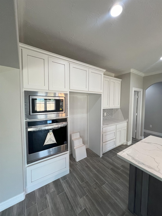 kitchen with light stone counters, wood finish floors, arched walkways, appliances with stainless steel finishes, and white cabinetry