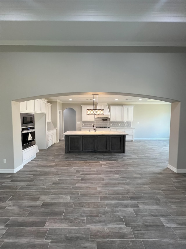 kitchen featuring tasteful backsplash, a center island with sink, white cabinets, appliances with stainless steel finishes, and light countertops