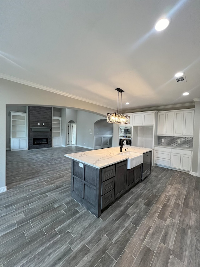 kitchen with arched walkways, a center island with sink, visible vents, white cabinetry, and a sink