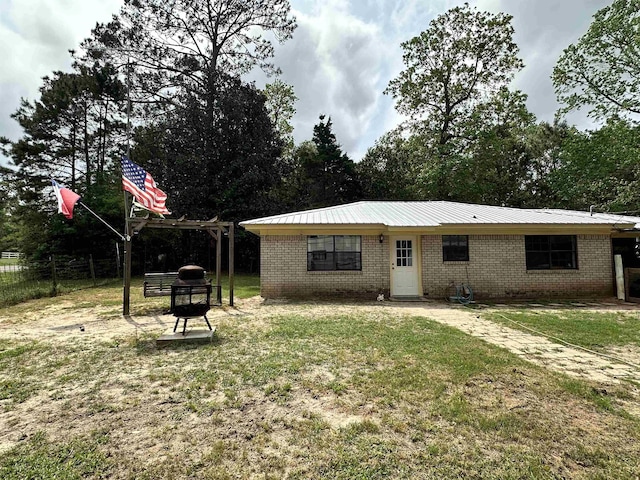 back of house featuring metal roof, fence, brick siding, a lawn, and a pergola