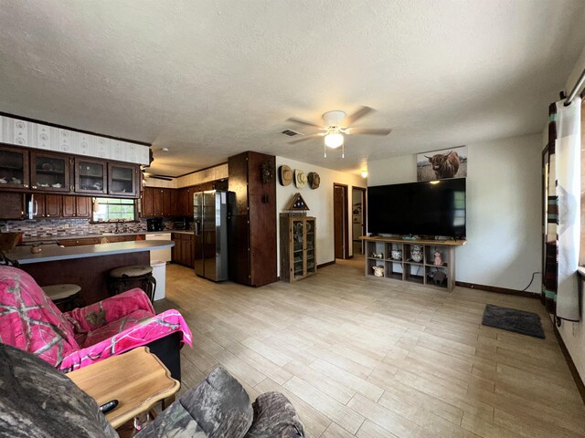 living area with a ceiling fan, a textured ceiling, baseboards, visible vents, and light wood-style floors