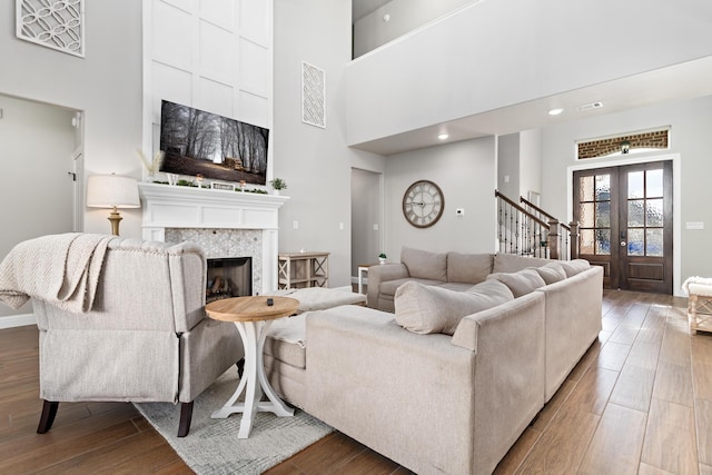 living room with wood-type flooring, a tiled fireplace, a high ceiling, and french doors