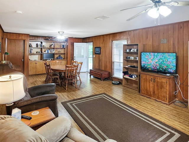 living area with a ceiling fan, wood finished floors, and wood walls