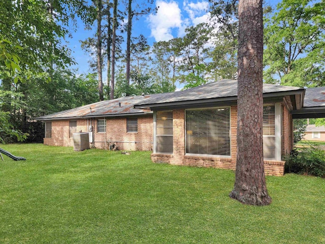 back of property featuring brick siding, central air condition unit, and a yard