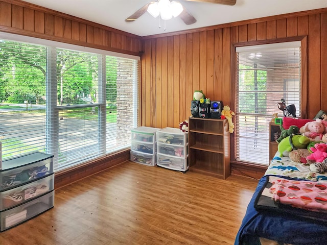 bedroom featuring a ceiling fan, wood finished floors, wooden walls, and multiple windows