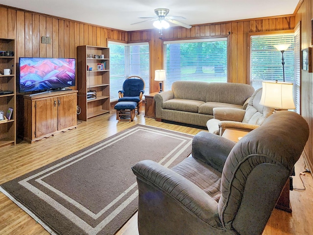 living area featuring plenty of natural light, wood walls, light wood-style floors, and a ceiling fan