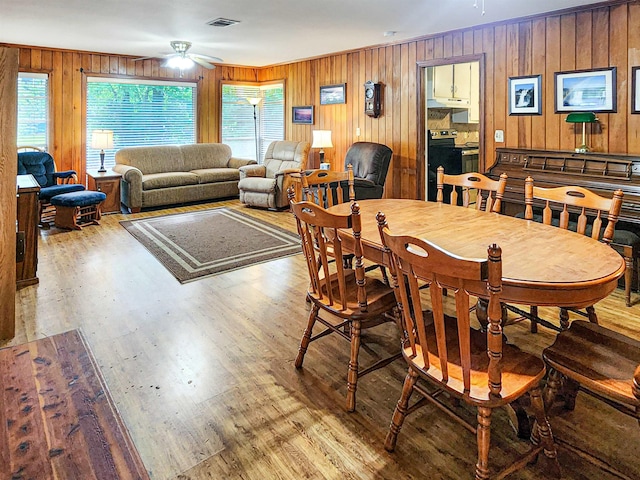 dining area featuring visible vents, ceiling fan, wood finished floors, and wooden walls