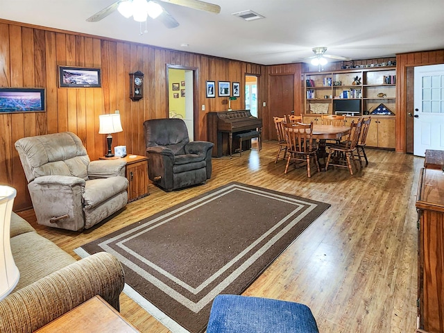 living room featuring a ceiling fan, wood walls, visible vents, and wood finished floors