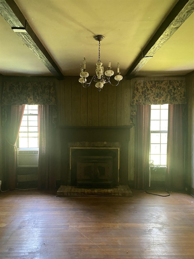 unfurnished living room with beamed ceiling, a wood stove, hardwood / wood-style flooring, and a chandelier