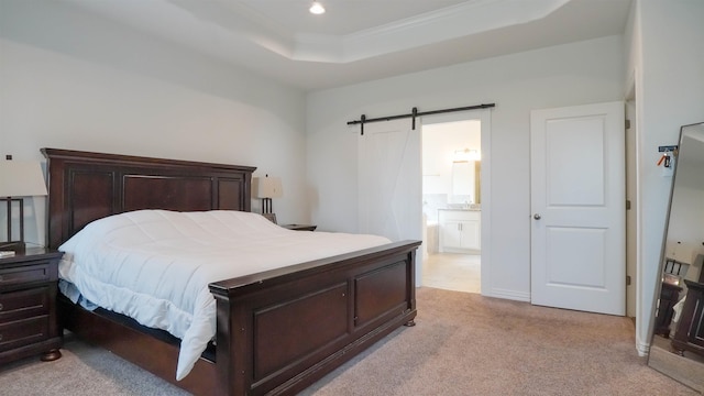 bedroom featuring a barn door, light colored carpet, connected bathroom, and a tray ceiling