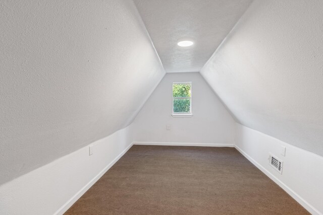 bonus room with a textured ceiling, dark carpet, and lofted ceiling