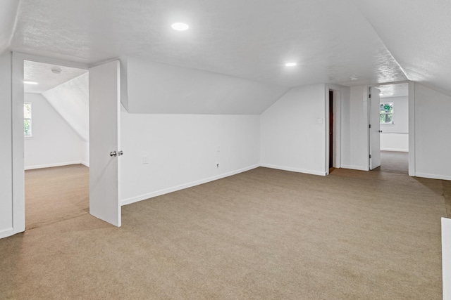 bonus room with a textured ceiling, light colored carpet, and vaulted ceiling