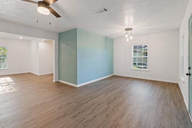 empty room with a textured ceiling, ceiling fan with notable chandelier, and hardwood / wood-style flooring