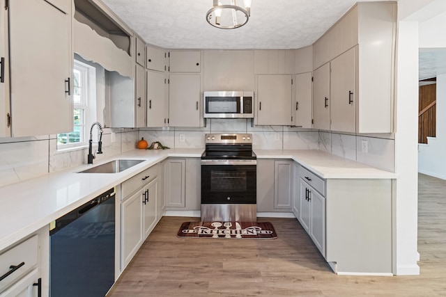 kitchen featuring appliances with stainless steel finishes, light wood-type flooring, backsplash, a textured ceiling, and sink