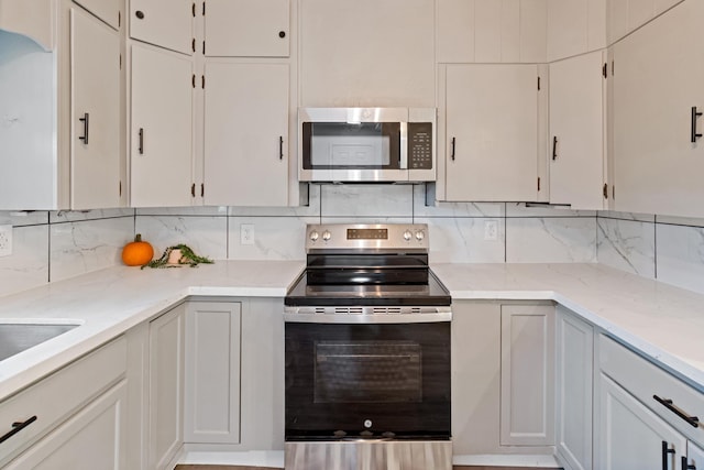 kitchen with white cabinets, light stone counters, appliances with stainless steel finishes, and tasteful backsplash