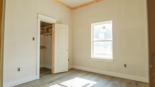 unfurnished bedroom with crown molding, wood finished floors, a closet, a spacious closet, and baseboards