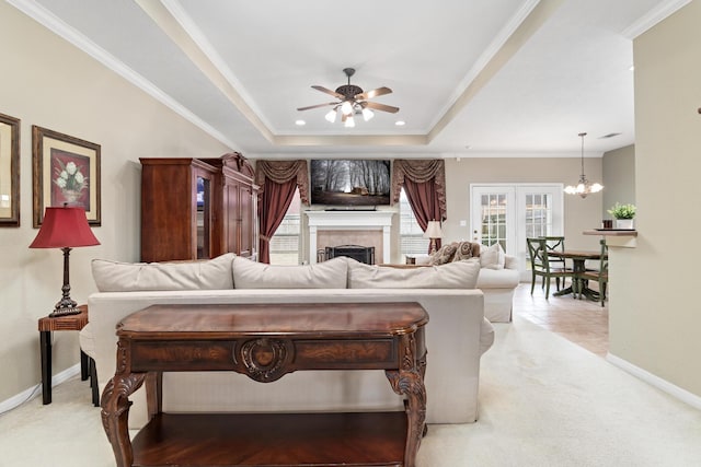 living room featuring crown molding, a tray ceiling, light colored carpet, a fireplace, and ceiling fan with notable chandelier