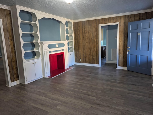 unfurnished living room featuring wood walls, dark hardwood / wood-style flooring, ornamental molding, a textured ceiling, and built in shelves