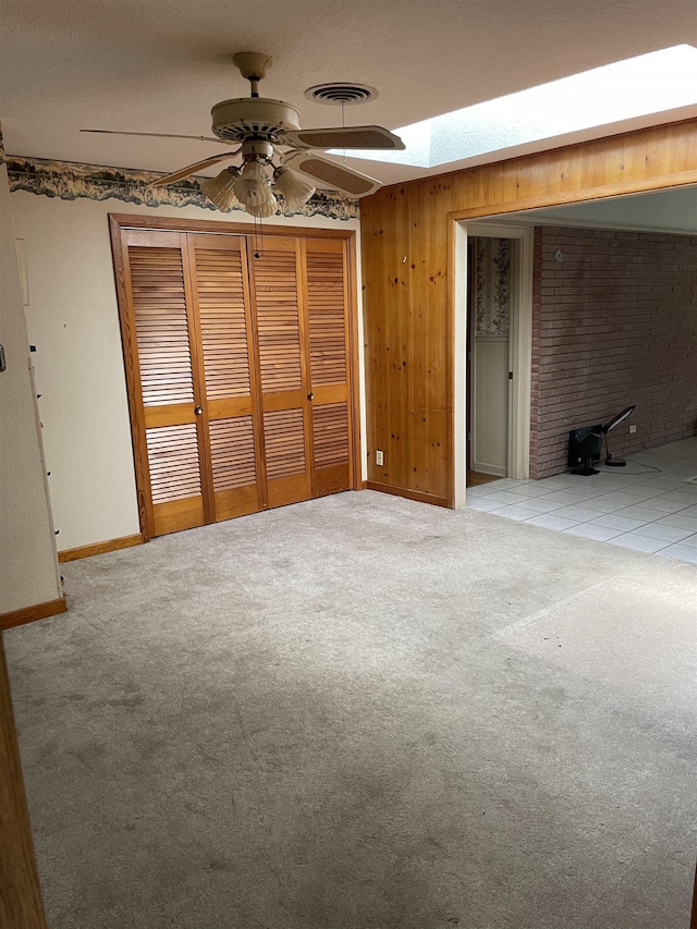 unfurnished bedroom with visible vents, a closet, carpet floors, wooden walls, and a skylight