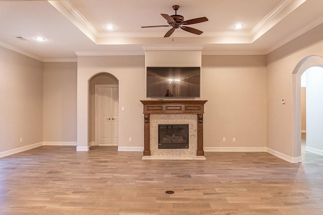 unfurnished living room featuring a raised ceiling, ceiling fan, light hardwood / wood-style flooring, and a high end fireplace